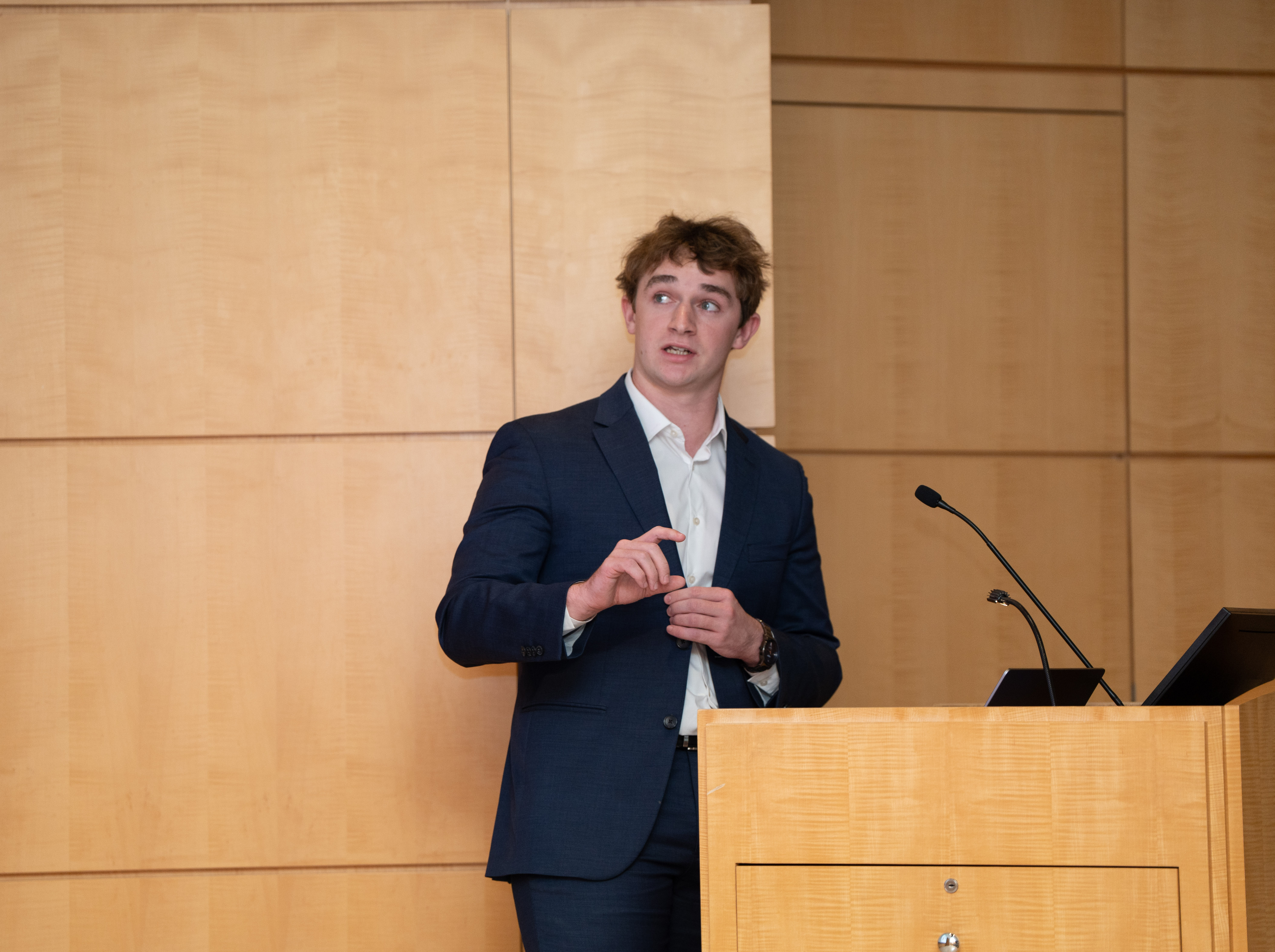 Ian Fairfield presents at the CanSUR Symposium at a podium in front of a wooden walk