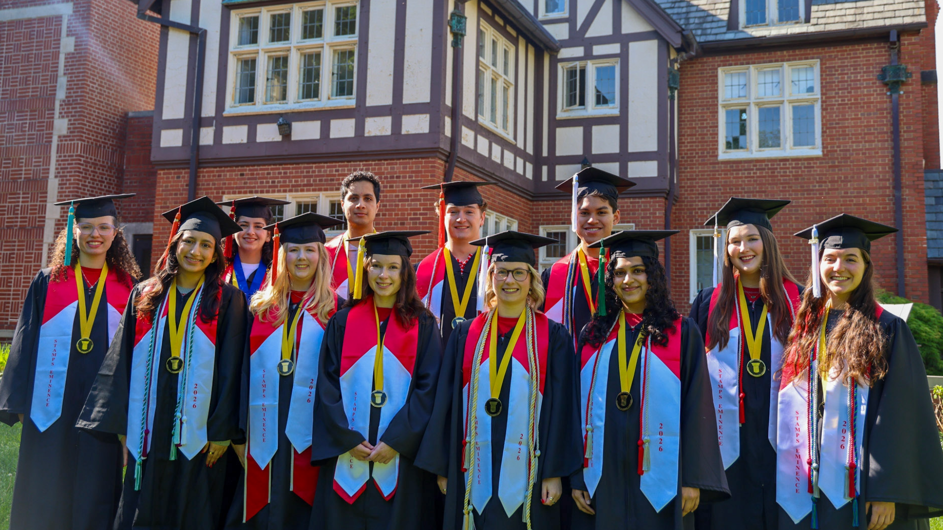 Stamps Eminence class of 2026 stand in front of Kuhn House wearing caps, gowns, and medals.
