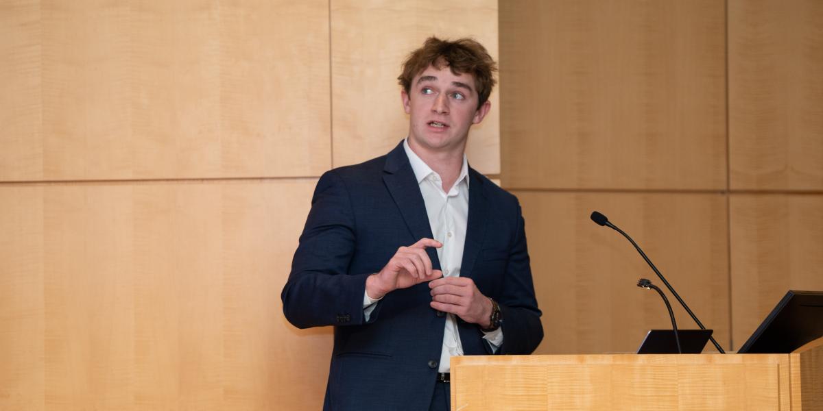 Ian Fairfield presents at the CanSUR Symposium at a podium in front of a wooden walk