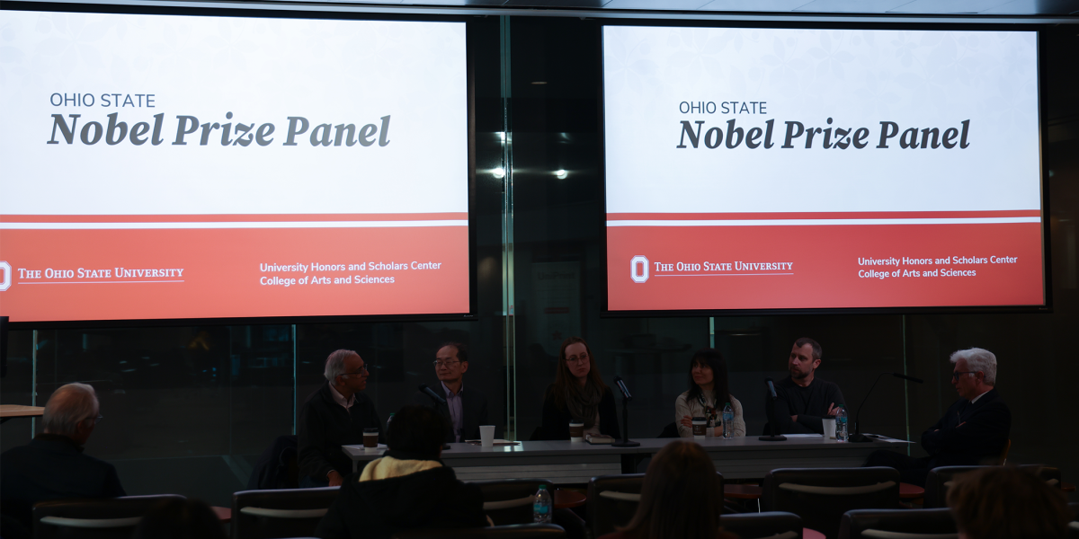 Two Nobel Prize Panel slides overlook crowd of peoplena several panelists