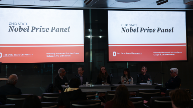 Two Nobel Prize Panel slides overlook crowd of peoplena several panelists