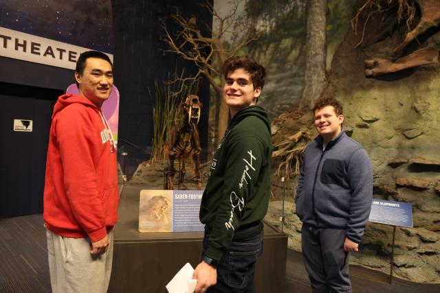 Scholars stand in from of an ice age model during a trip based on natural history and engineering