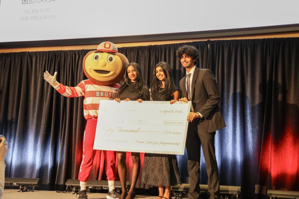 A group of people stand on stage with Brutus Buckeye presenting a large check for $50,000 made out to "Viera Wellness."