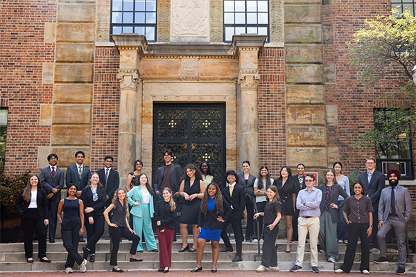 A group of people standing and posing in front of a large, ornate building entrance with brick and stone details.