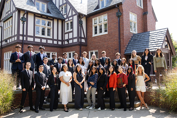 A group dressed in formal and casual attire stands in front of Tudor-style architecture.