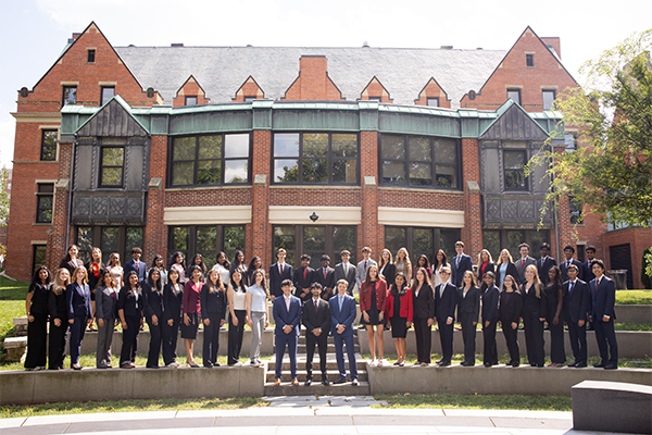 A large group in business attire stands in front of a historic brick building.