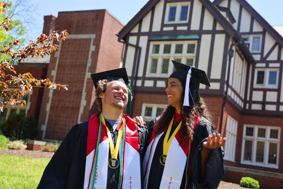 Two students in graduation regalia outside the Kuhn House