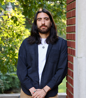 Portrait of Roman Suer leaning on brick wall with greenery in background